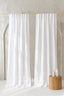 White curtains on a wooden rod against a neutral wall with a wooden stool and bottles.